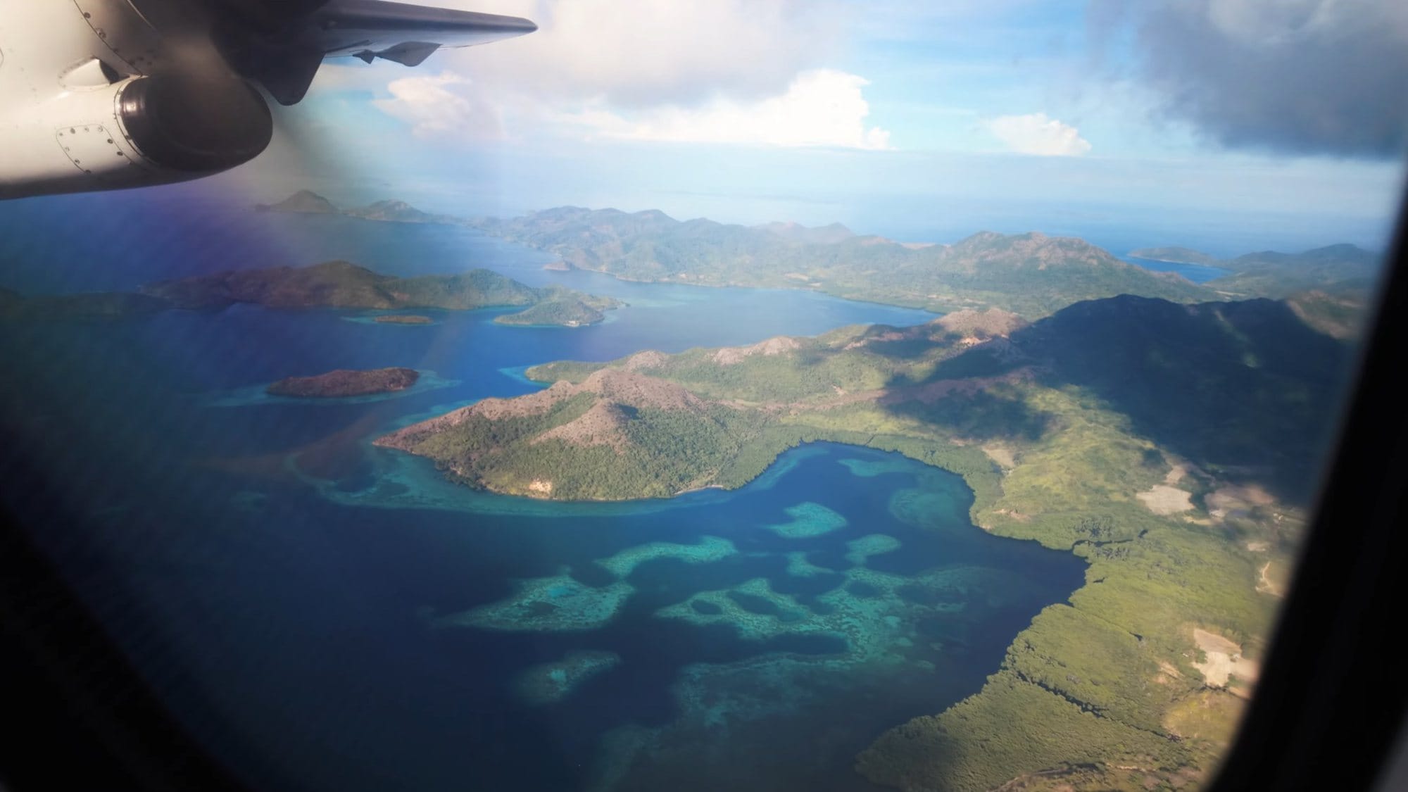 Islands and reefs seen past the propeller through the window of a small plane