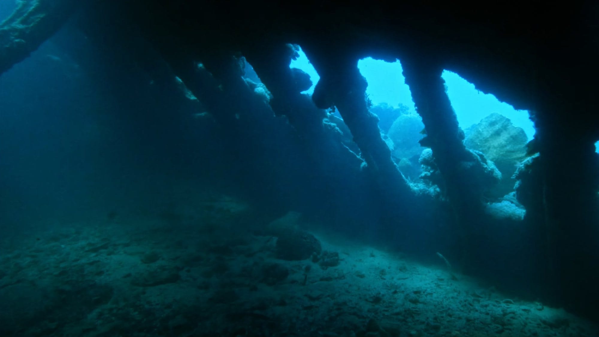 Inside a shipwreck, light falling through the gaps between its coral-covered ribs
