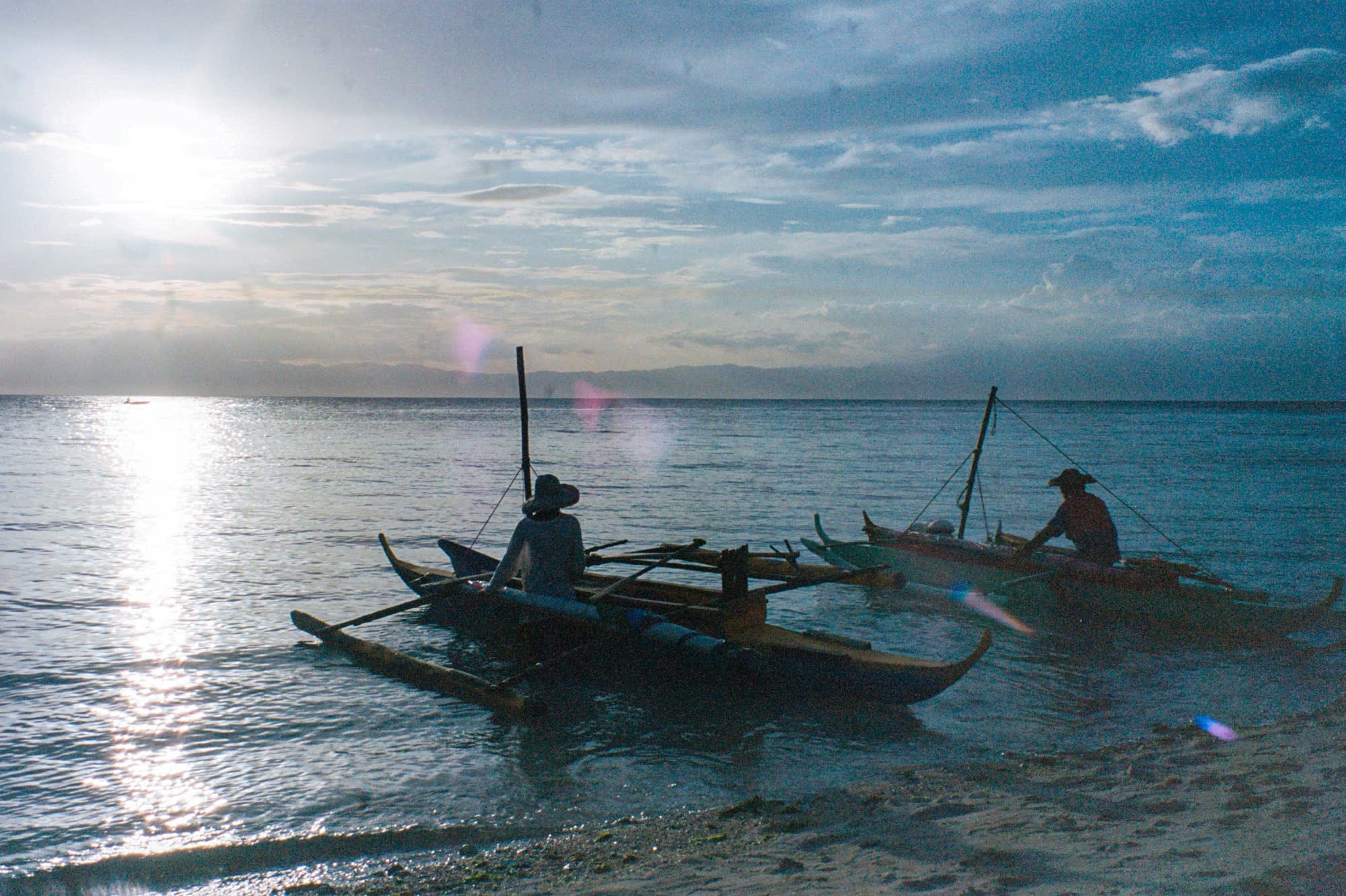 Two outrigger boats in the shallows at sunset, fishermen in hats aboard