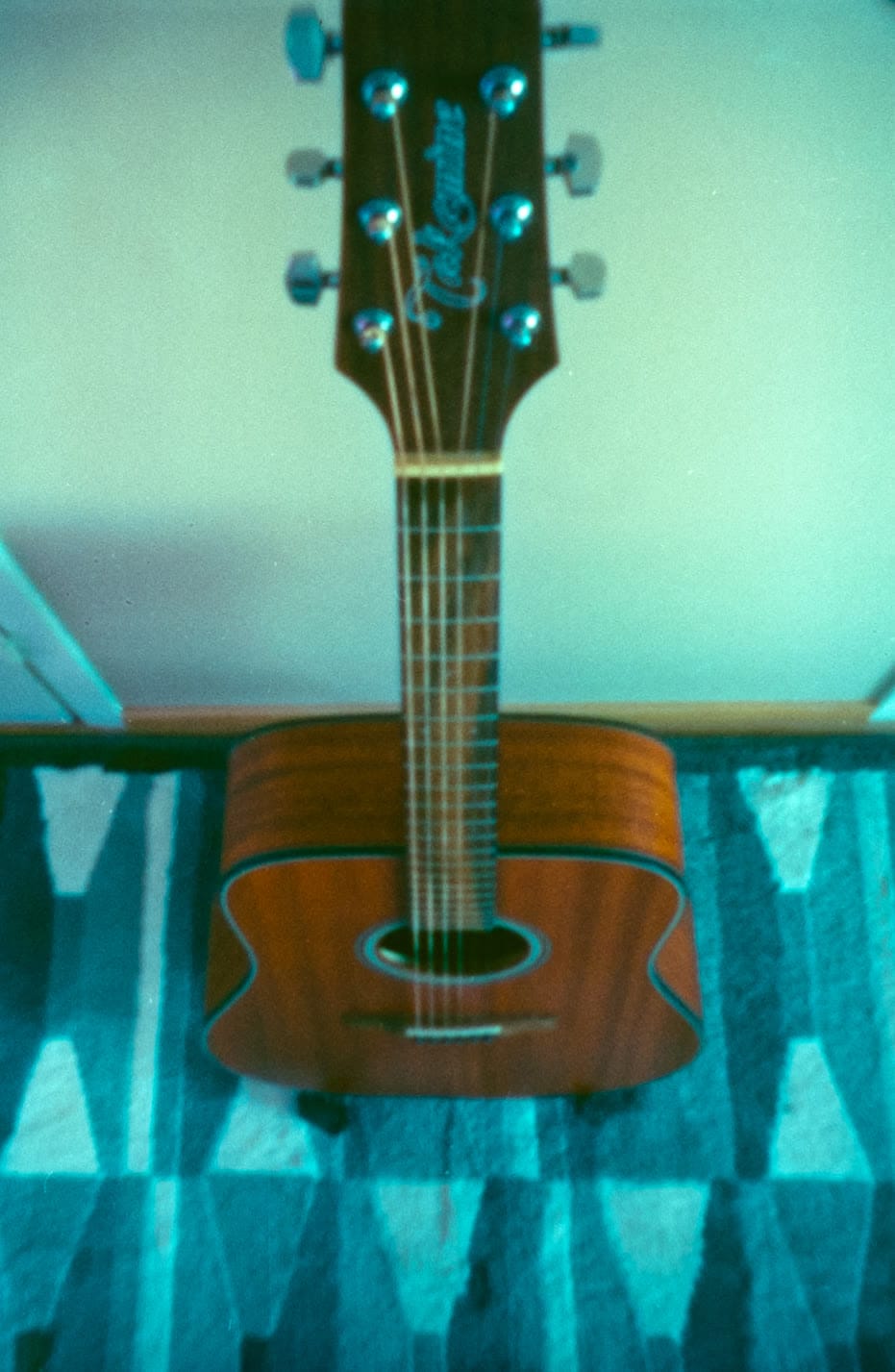 An acoustic guitar standing on a patterned blue rug, on film